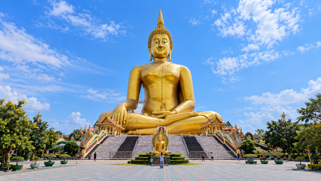 Stor siddende gylden Buddha ved Wat Muang med brede trapper, udsmykkede pavilloner og besøgende foran soklen.