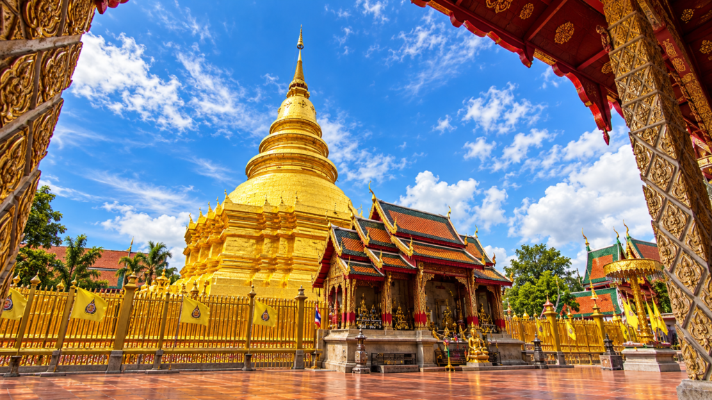 AI-genereret illustration af den gyldne chedi ved Wat Phra That Hariphunchai i Lamphun, set fra tempelgården.