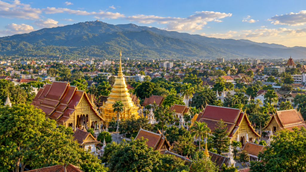 Illustreret udsigt over Chiang Mai med gyldne tempelspir, røde tage og bjerge i baggrunden.